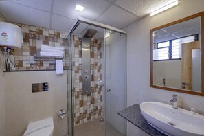 A bathroom with a glass shower enclosure, a sink, and a mirror. - Hotel CityInn (Gandhinagar)