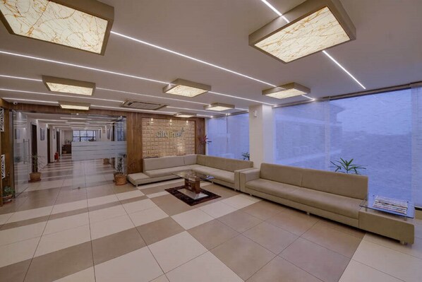 A modern hotel lobby with a checkered floor, a sofa, a coffee table, and a large window offering a view. - Hotel CityInn (Gandhinagar)