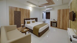 A modern hotel room with a large bed, a sofa, a small table, and a TV. - Hotel CityInn (Gandhinagar)