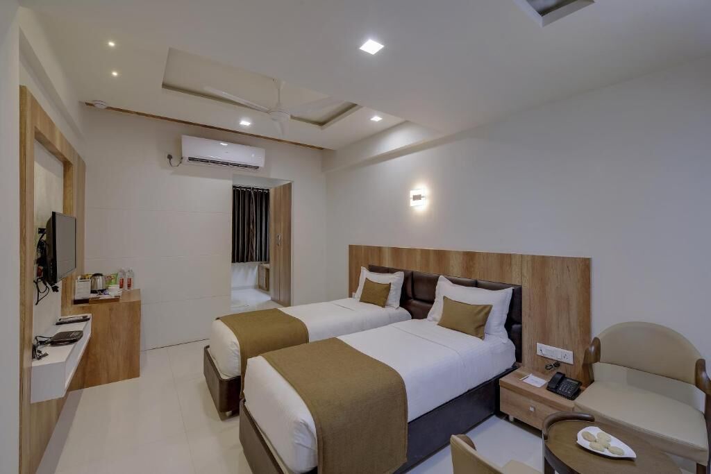 Habitación de hotel con dos camas, un escritorio con silla, una mesita con un plato y un televisor.
