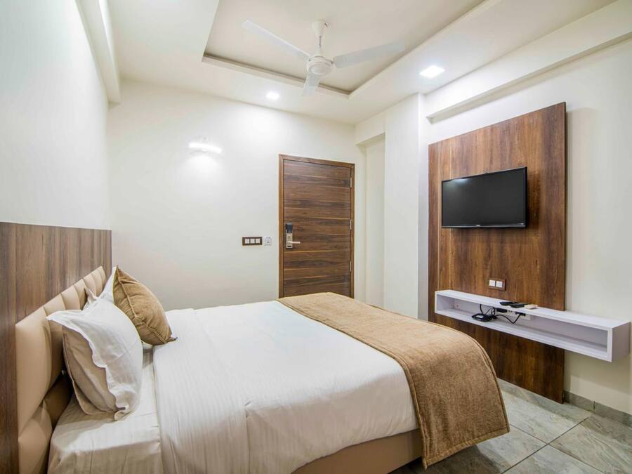 Un dormitorio con cama, ventilador de techo, televisor montado en un panel de madera y un estante pequeño debajo del televisor.