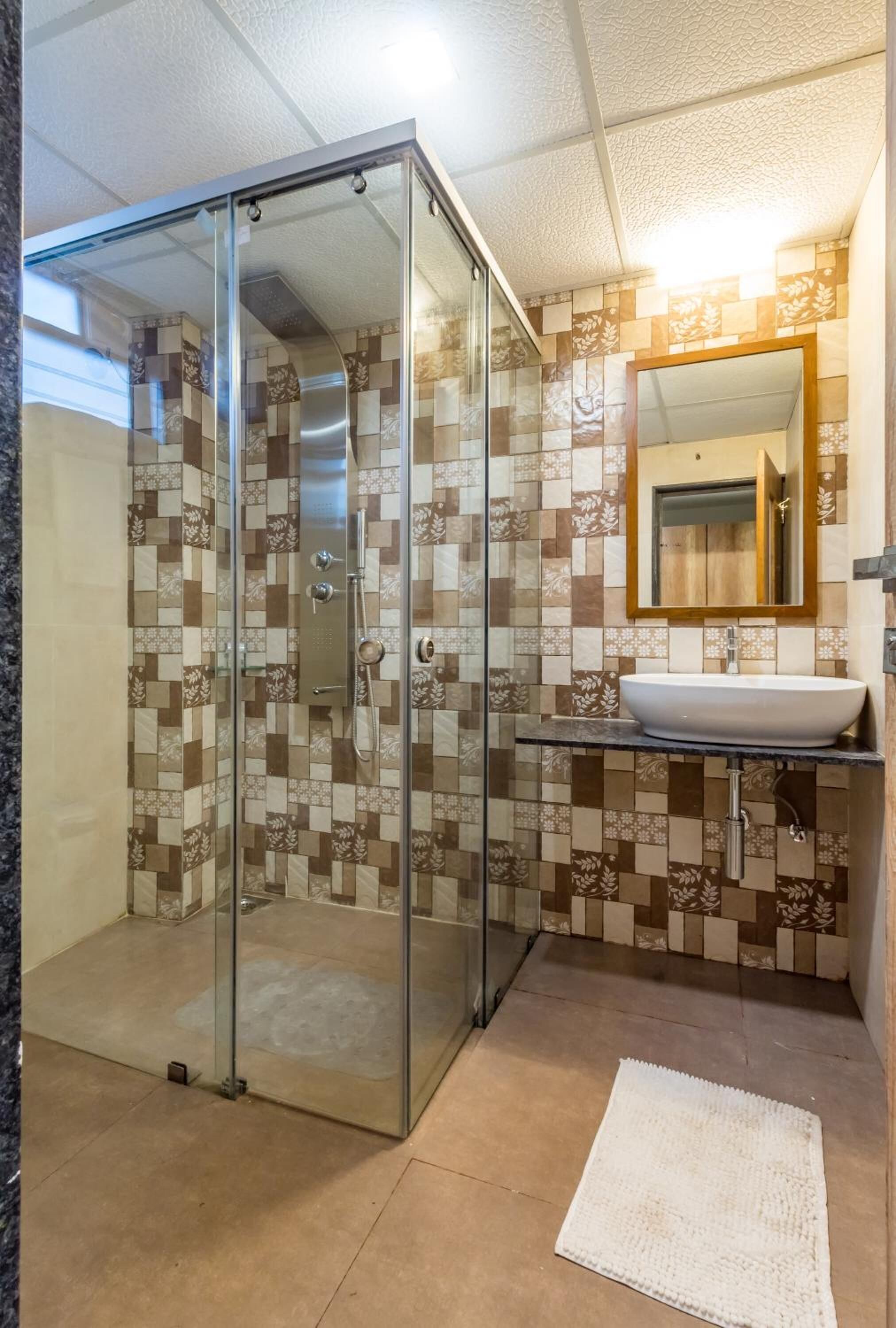 A bathroom with a glass-enclosed shower, a sink with a mirror, and patterned tile walls.