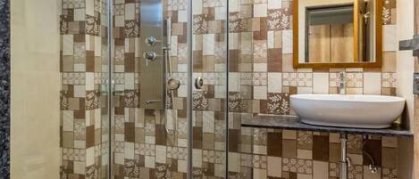 A bathroom with a glass-enclosed shower, a sink with a mirror, and patterned tile walls.