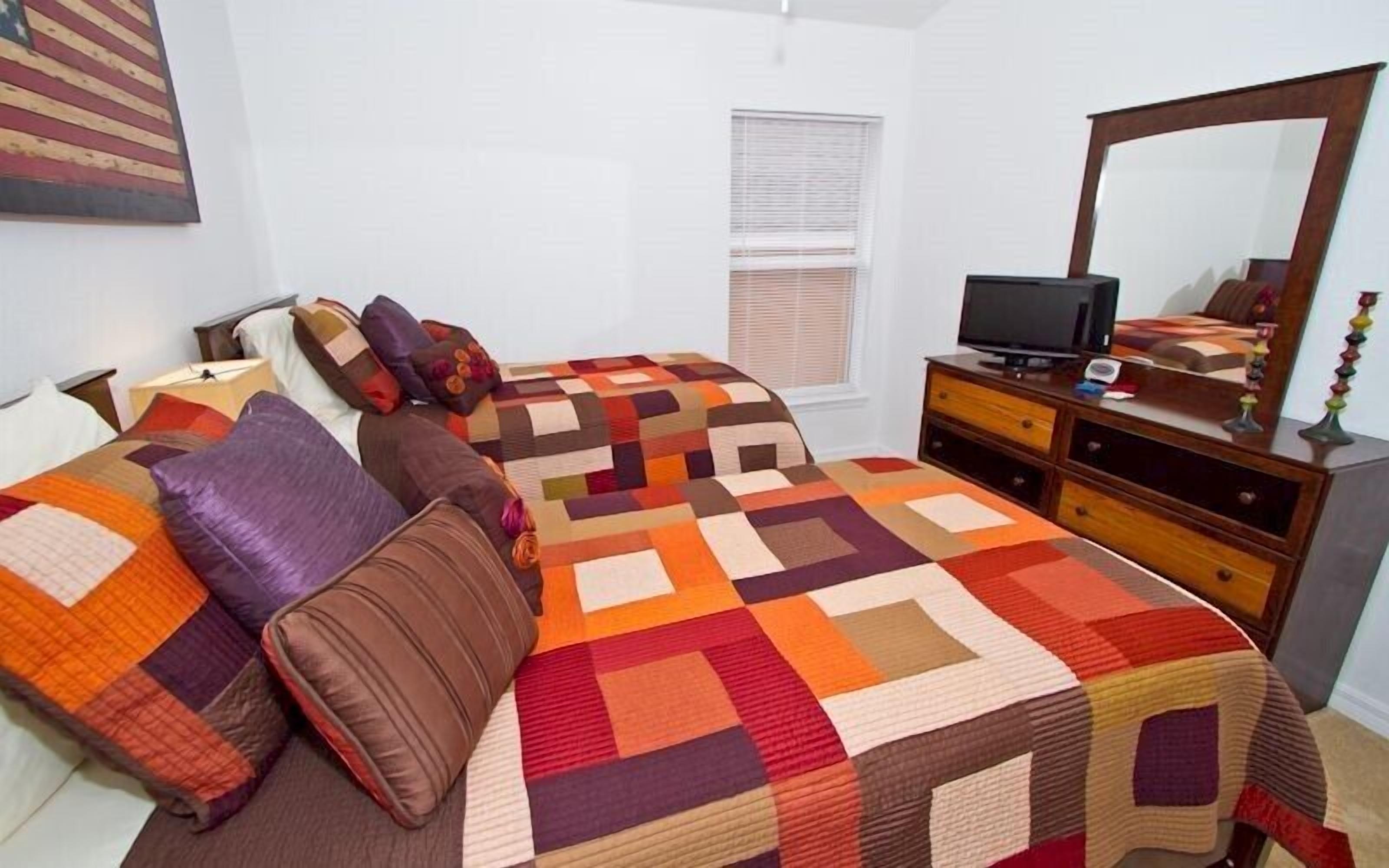 A bedroom with a bed, a dresser, a television, and a window with blinds.