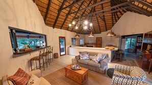 A spacious living area with a high ceiling, a wooden coffee table, a sofa, and a patterned armchair. - Nyala Safari Lodge (Hoedspruit)