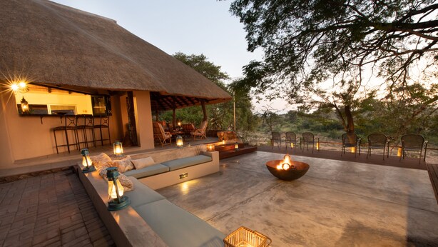 An outdoor seating area with a thatched-roof structure, cushioned seating, and a fire pit. - Nyala Safari Lodge (Hoedspruit)