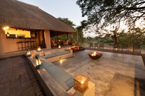 An outdoor seating area with a thatched-roof structure, cushioned seating, and a fire pit. - Nyala Safari Lodge (Hoedspruit)