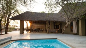 A pool area with a thatched-roof pavilion, wooden deck, and outdoor furniture. - Nyala Safari Lodge (Hoedspruit)