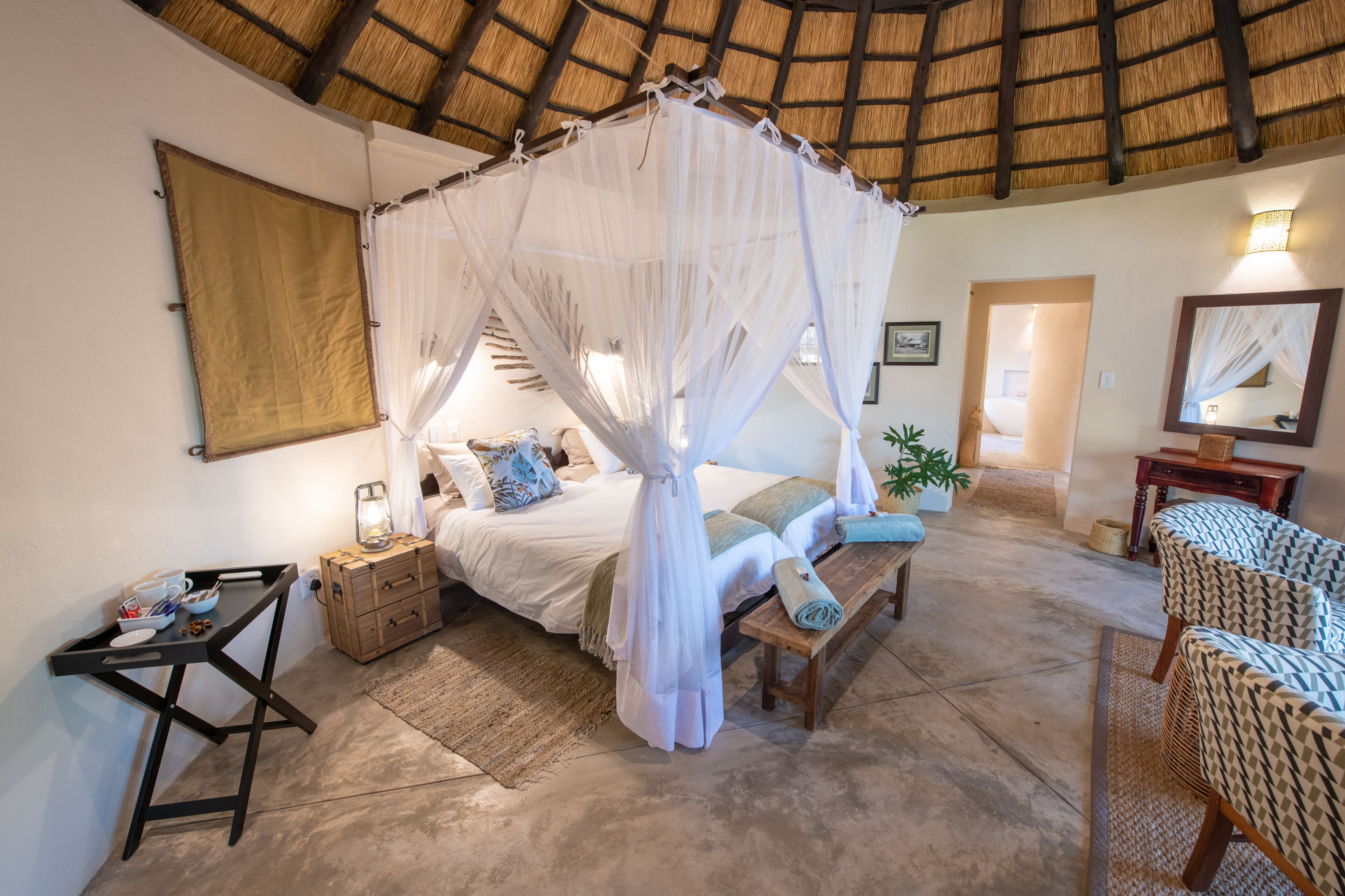 A room with a bed under a canopy, a wooden bench, a small table, and a chair.