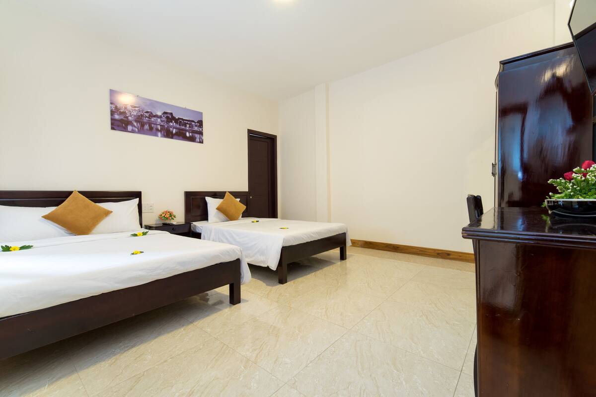 A hotel room with two beds, a flat-screen TV, a wooden cabinet, and a cityscape painting on the wall.