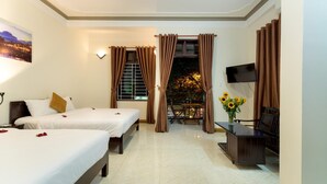 Habitación de hotel con dos camas, televisor, mesa de comedor con sillas y balcón con flores.