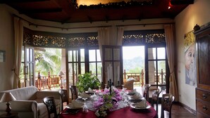 A dining area with a round table set for four, surrounded by chairs, with a view of palm trees through large windows. - Gunung Paradis Retreat (Seririt)
