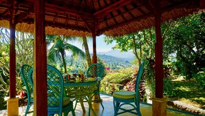 A covered outdoor seating area with a table and chairs, surrounded by lush greenery and a view of the landscape. - Gunung Paradis Retreat (Seririt)