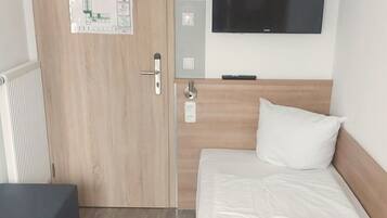 Hotellihuone, jossa on sänky, seinälle asennettu televisio, ovessa oleva kartta ja pieni pöytä.