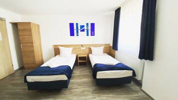 Une chambre d’hôtel avec deux lits simples, une armoire en bois, une petite table et une œuvre d’art accrochée au mur.