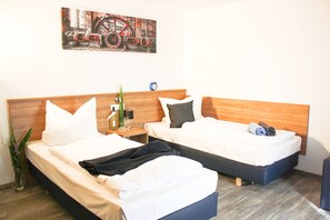 A hotel room with two beds, wooden headboards, white bedding, a small bedside table with a lamp, and a wall-mounted artwork. - Sunny Hotel (Aiterhofen)