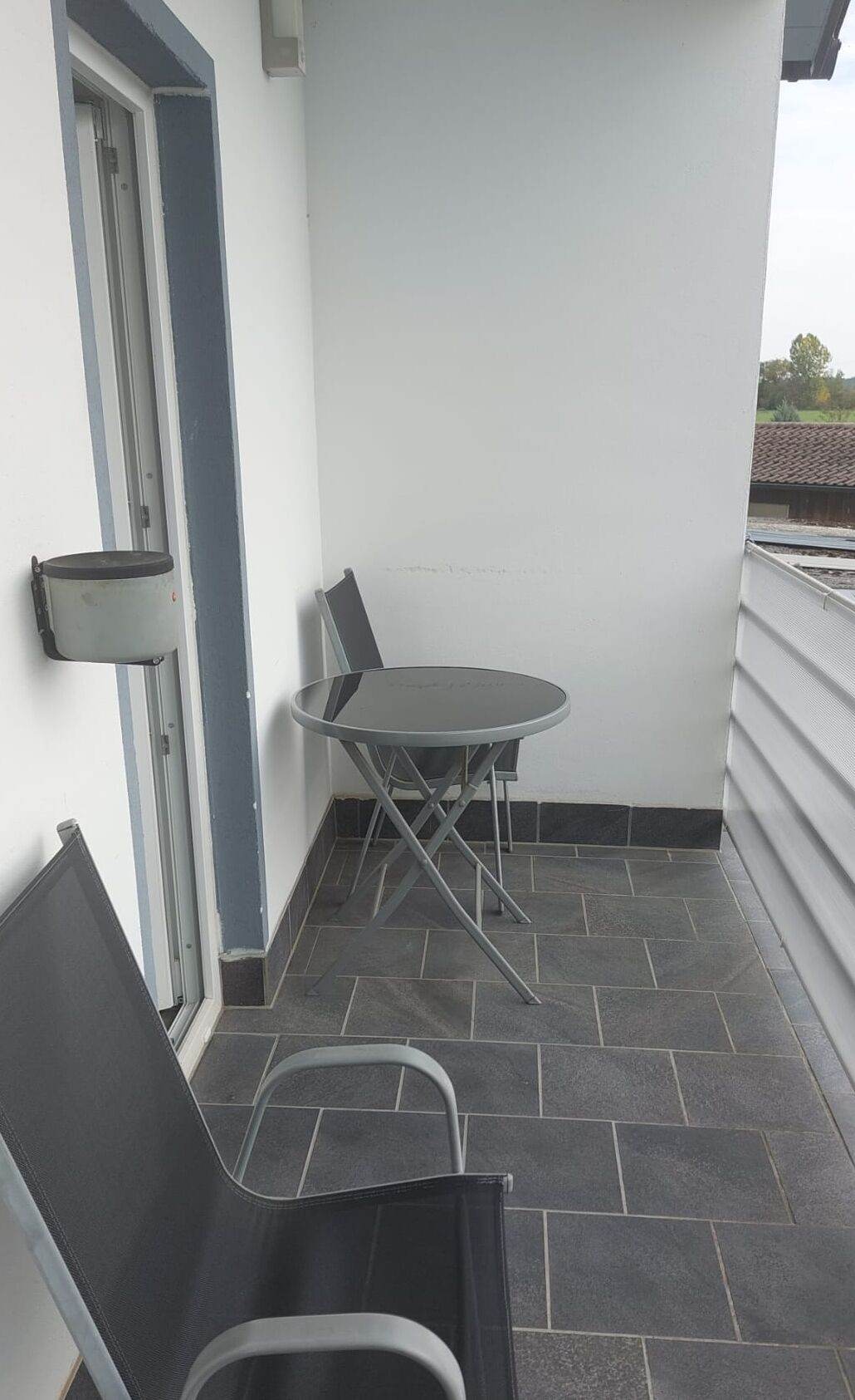 Un pequeño balcón con mesa y sillas, una puerta y vistas al exterior.