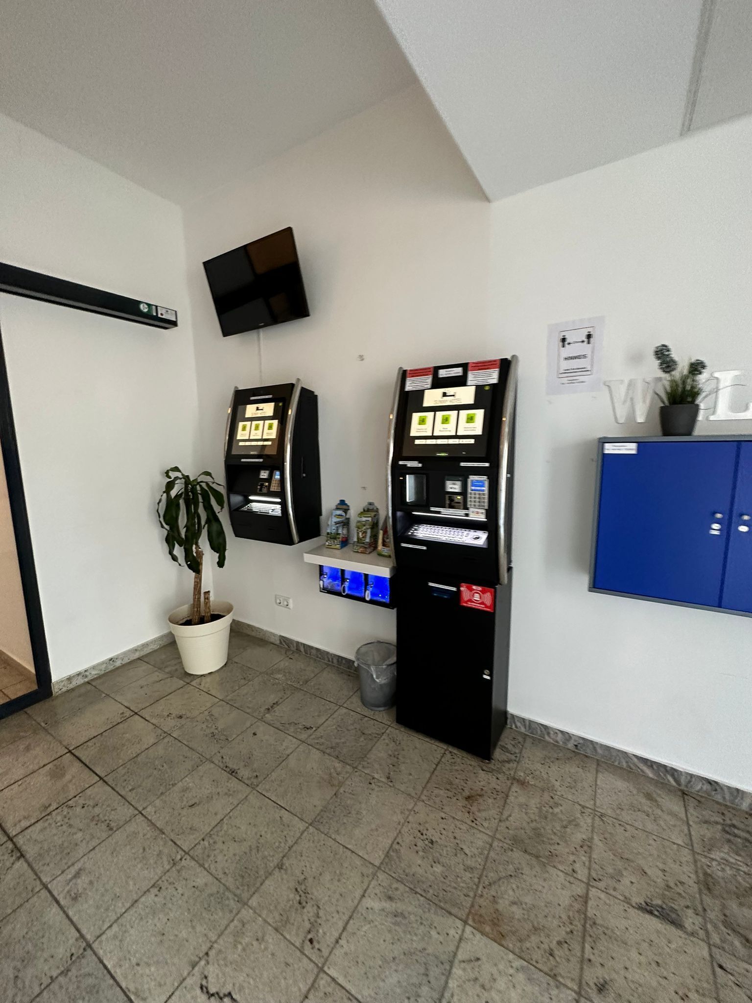 A reception area with two ATMs, a potted plant, a blue cabinet, and a mounted television.