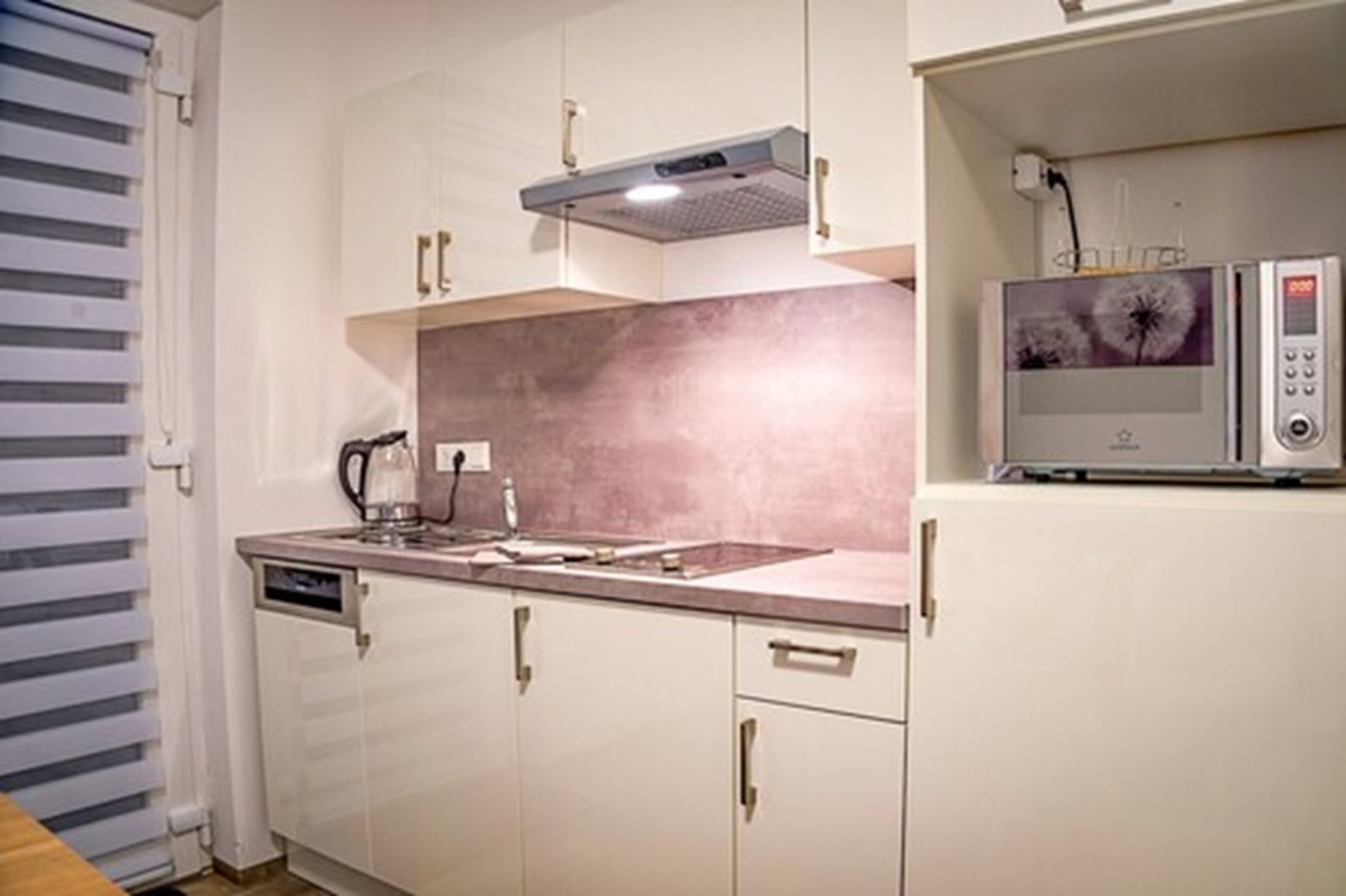 A kitchen with white cabinets, a stainless steel range hood, a microwave, and a coffee maker.