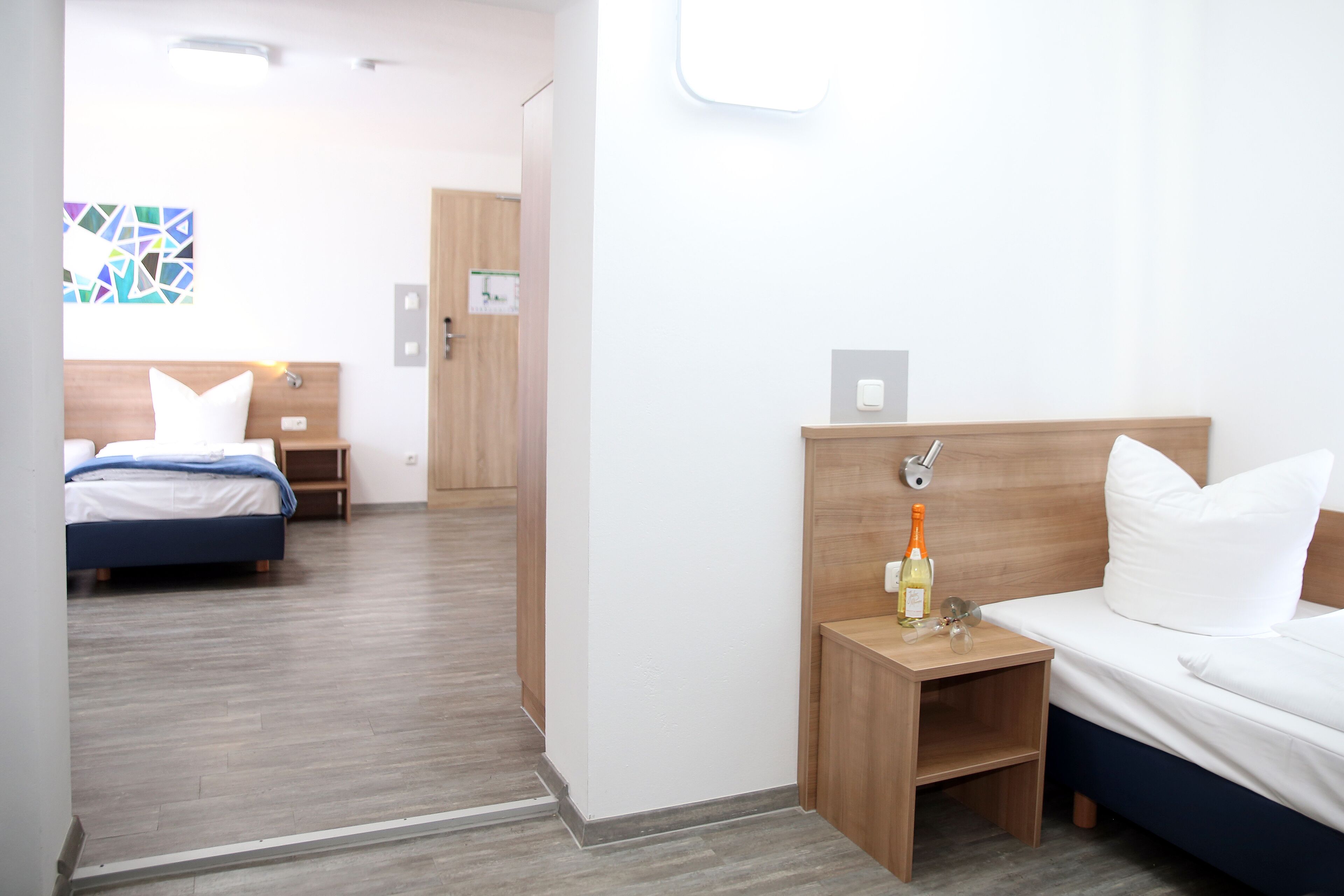 A hotel room with a bed, bedside table, and a mirror. There is a door leading to another room.