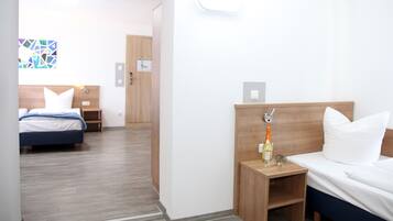 A hotel room with a bed, bedside table, and a mirror. There is a door leading to another room.