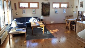 A cozy living room with a sofa, coffee table, and dining table, wooden floors, and large windows. - Holiday Home Fjätervålen Fjätstigen (Sarna)