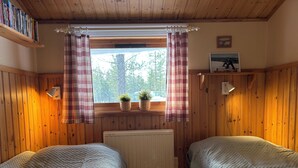 A cozy room with wooden walls, two beds with quilts, a window with plaid curtains, and a radiator. - Holiday Home Fjätervålen Fjätstigen (Sarna)