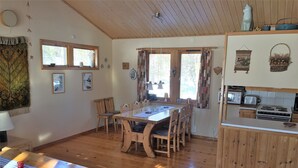 A cozy, well-lit dining area with a wooden table and chairs, a kitchen with basic appliances, and large windows allowing natural light. - Holiday Home Fjätervålen Fjätstigen (Sarna)