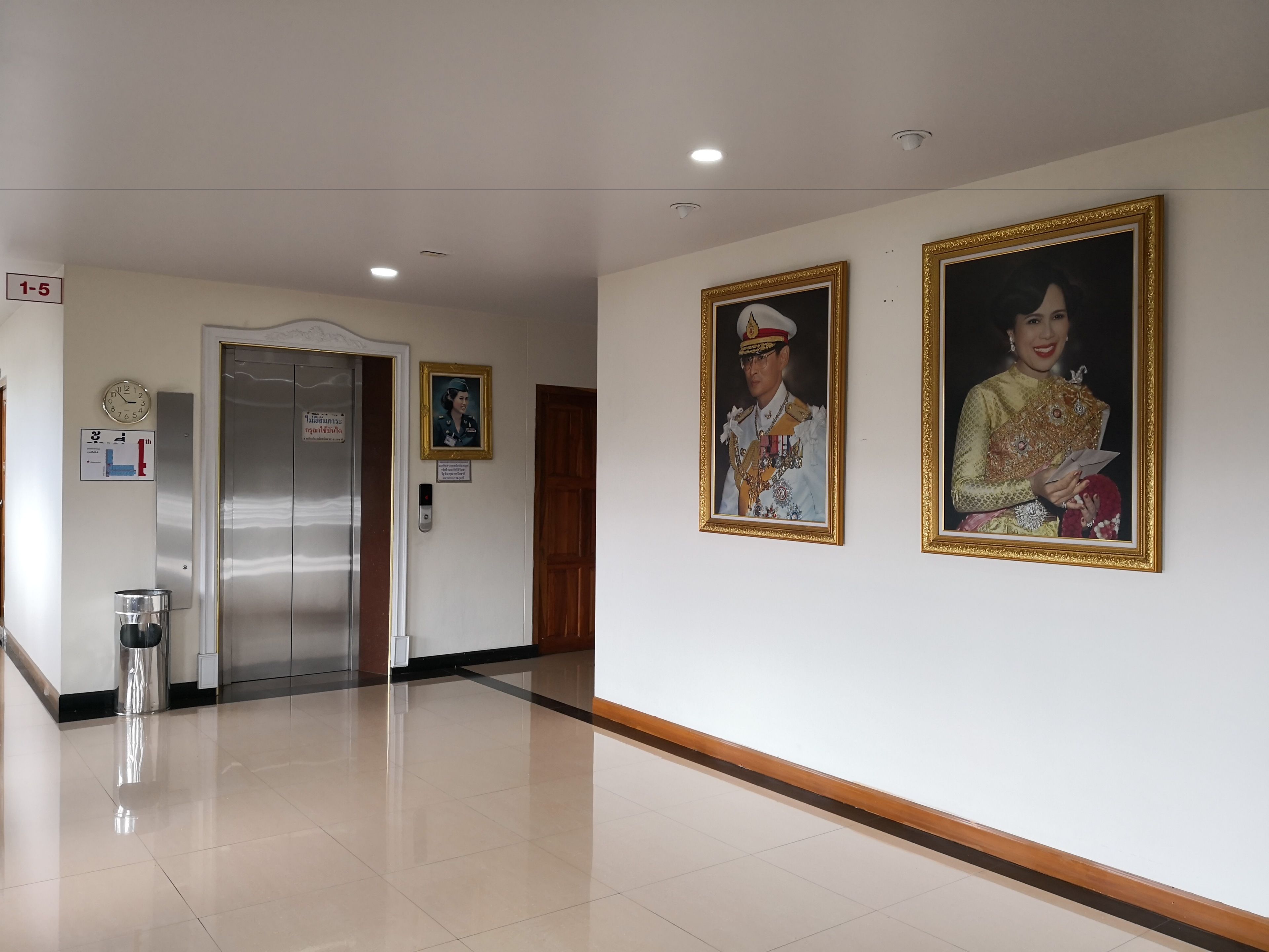 Un couloir doté d’un plancher poli, d’un ascenseur et de deux portraits encadrés accrochés au mur.
