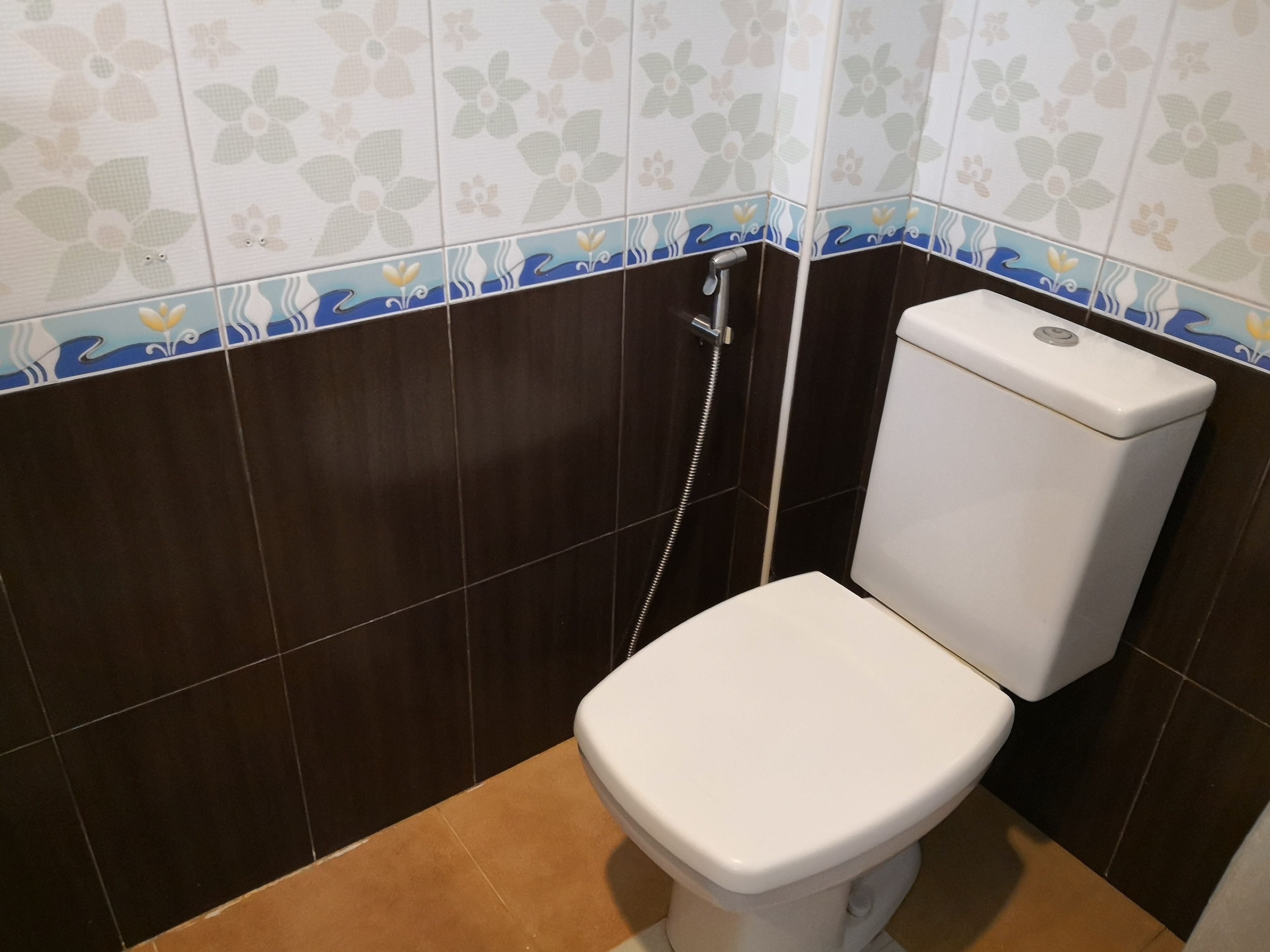 A small bathroom with a toilet, a shower, and a wall with floral tile design.
