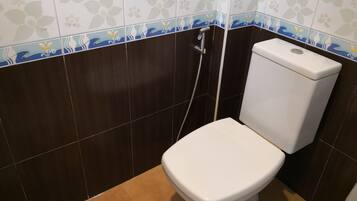 A small bathroom with a toilet, a shower, and a wall with floral tile design.