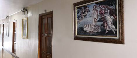 A hallway with a polished floor, wooden doors, and framed artwork on the walls.