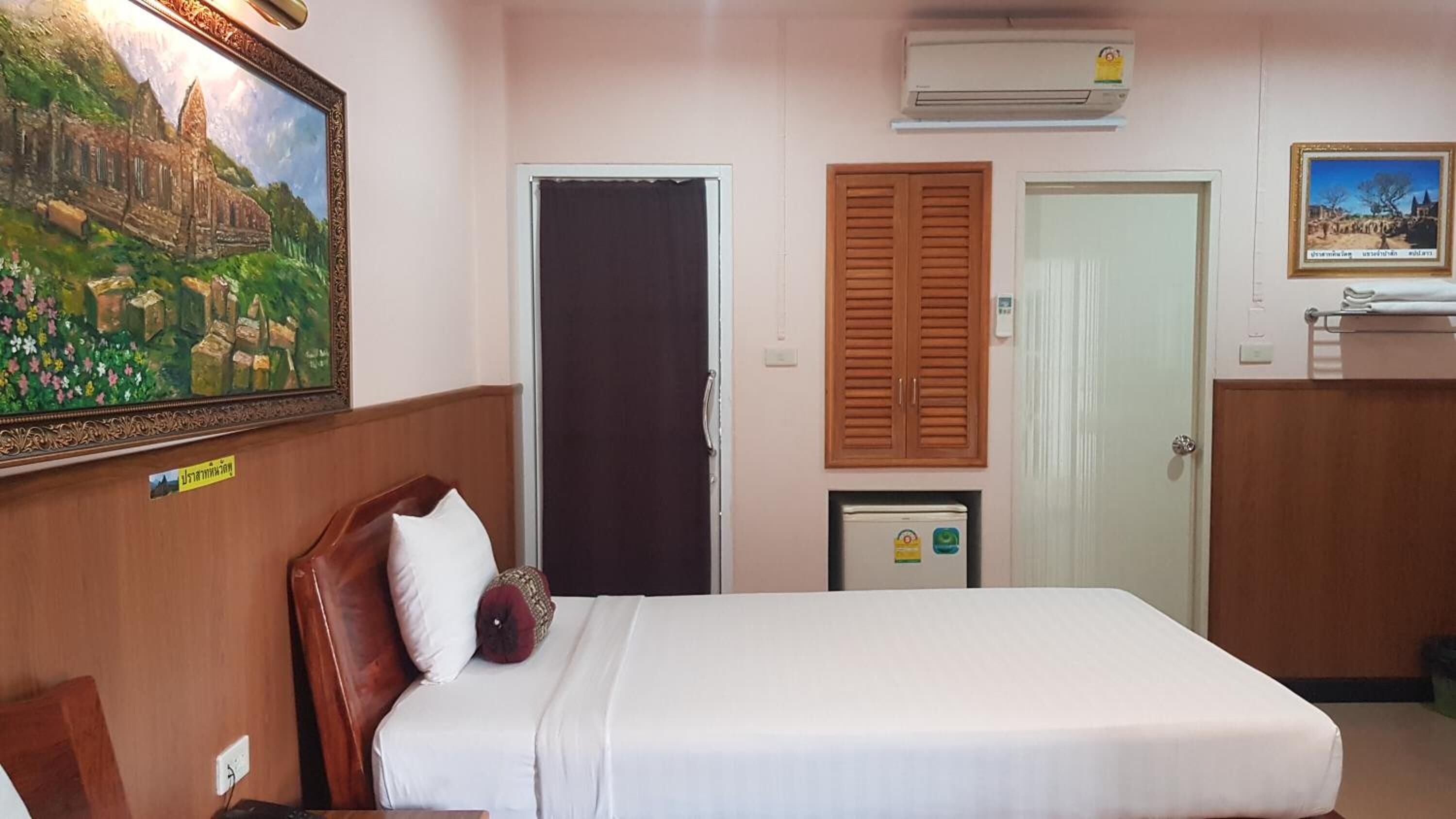 A hotel room with a bed, a door, a small refrigerator, and a wall-mounted air conditioner.