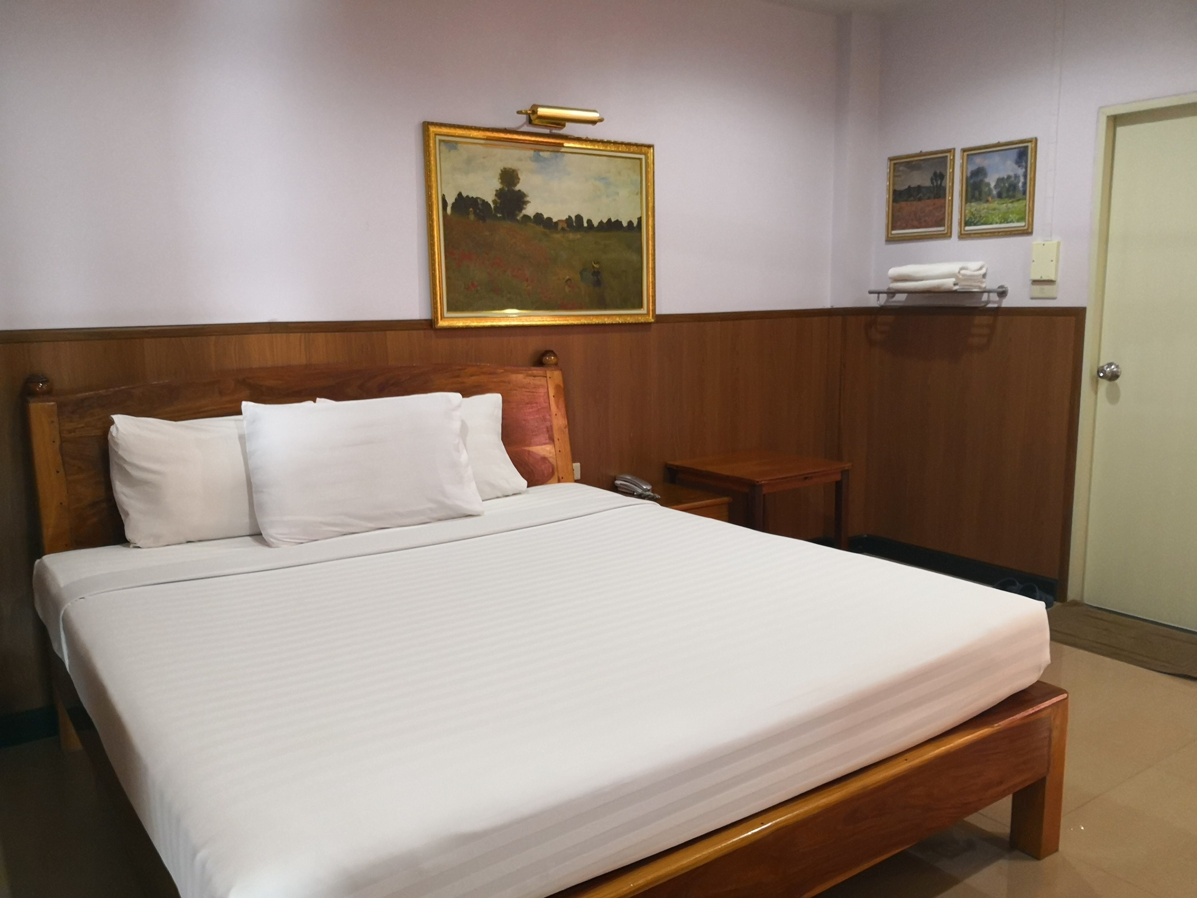 Een hotelkamer met een houten bed, witte lakens, een houten hoofdbord, een nachtkastje met telefoon en een schilderij aan de muur.