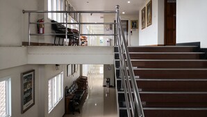 A multi-level hotel lobby with a staircase, seating areas, and framed artwork on the walls. - Phadaeng Hotel (Ubon Ratchathani)