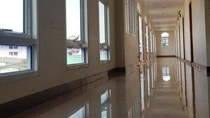 A long, well-lit hallway with large windows on one side and doors on the other. - Phadaeng Hotel (Ubon Ratchathani)