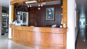 A reception area with a wooden counter, a clock, a framed artwork, and a refrigerator in the background. - Phadaeng Hotel (Ubon Ratchathani)