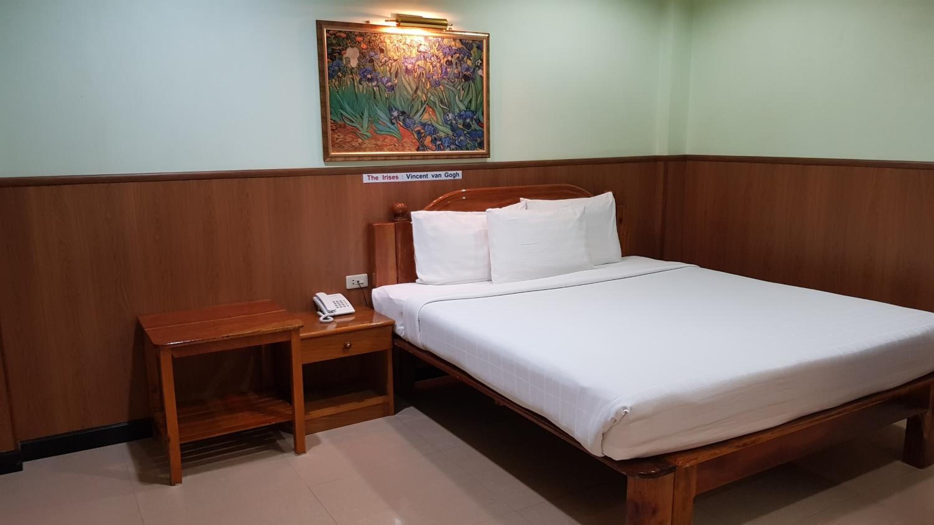 A hotel room with a wooden bed, a nightstand with a phone, and a painting of irises on the wall.