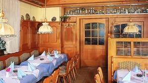 Uma área de refeições com mesas grandes, cadeiras de madeira e teto decorativo.