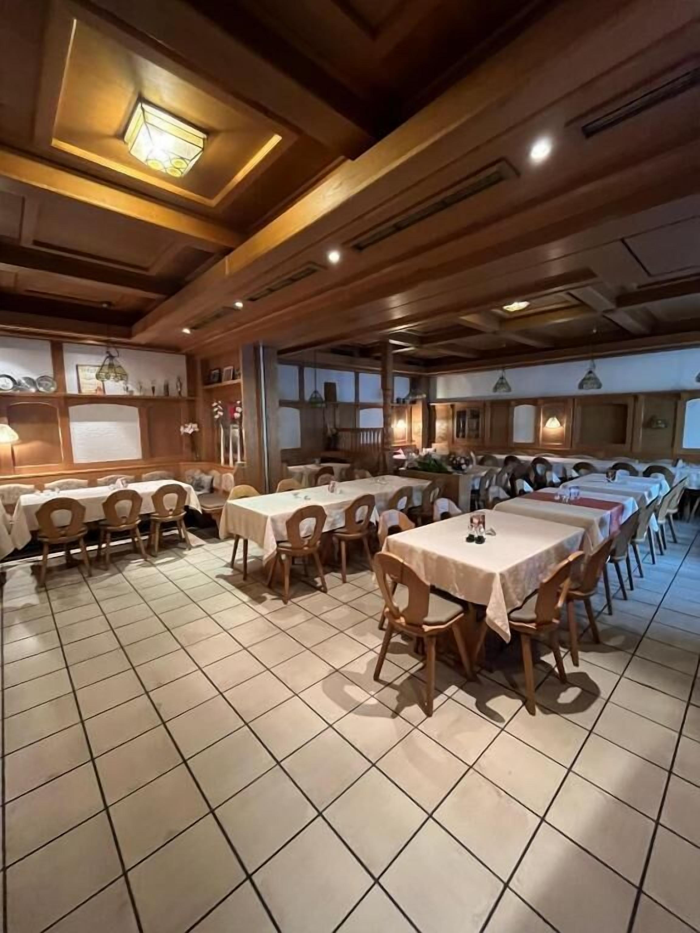 Een eetruimte met meerdere tafels en stoelen, houten balken in het plafond en inbouwspots.