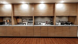 A modern kitchen with wooden cabinets, a stainless steel countertop, and various appliances. - TownePlace Suites by Marriott Louisville Airport (Louisville)