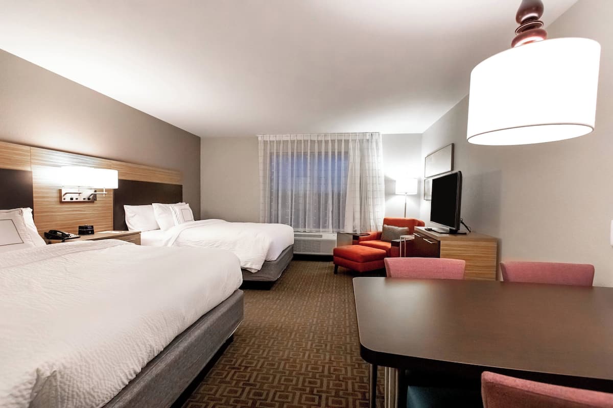 A hotel room with two beds, a desk, a television, and a window with curtains.