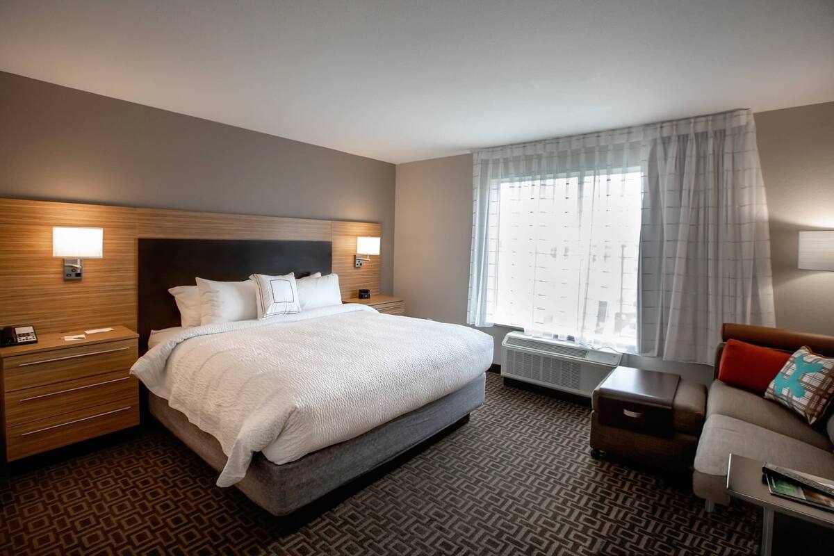 A hotel room with a large bed, bedside tables, a sofa, and a window with curtains.