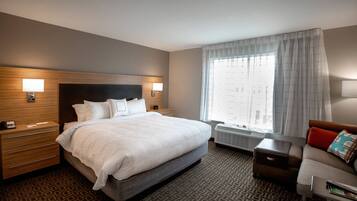 A hotel room with a large bed, bedside tables, a sofa, and a window with curtains.