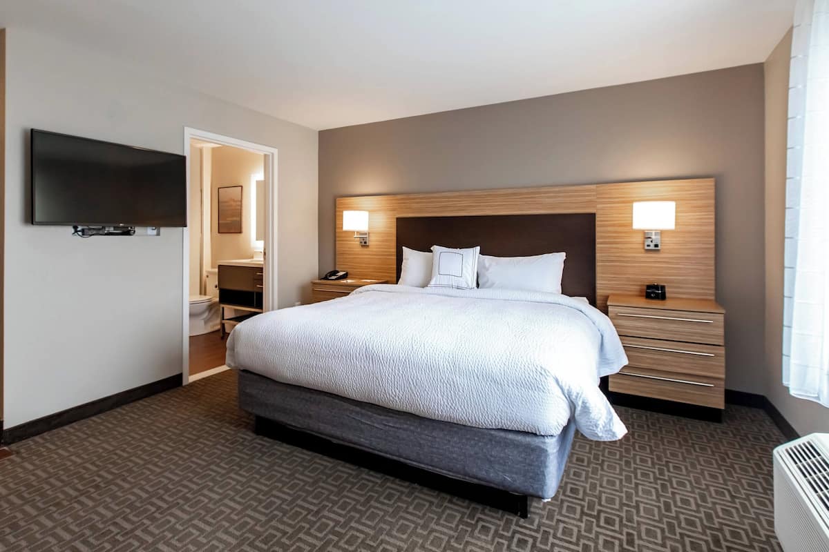 A hotel room with a large bed, bedside tables, a flat-screen TV, and a bathroom visible through an open door.