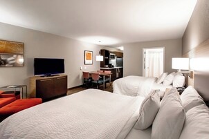 Habitación de hotel con dos camas, televisión, escritorio y kitchenette.