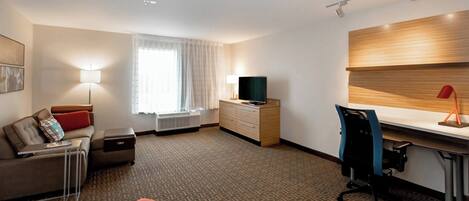 A modern hotel room with a sofa, a desk, a chair, a TV, a dresser, and a window with curtains.