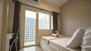 Quarto de hotel com cama, escrivaninha e janela com cortinas.
