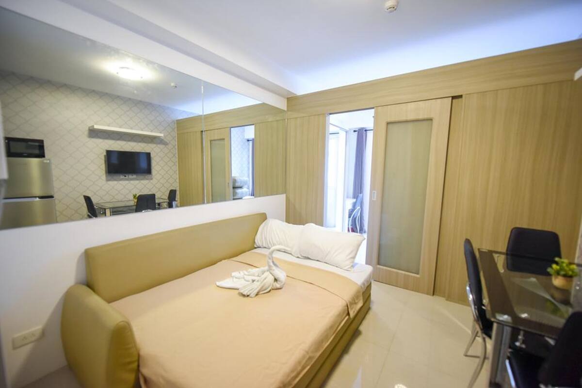 Quarto de hotel moderno com cama, sofá, mesa de jantar e televisão.