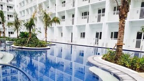 Um hotel moderno com uma grande piscina interior, rodeado por varandas brancas e palmeiras.